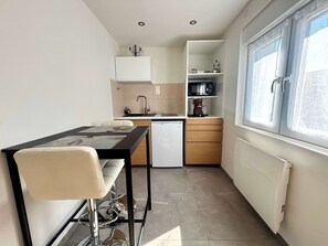 Una cucina funzionale con zona pranzo, frigorifero, forno a microonde e finestra con tende.