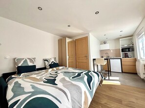 Una camera da letto con un letto, due cuscini, un comodino e una scrivania con una sedia. Si trova anche un armadio in legno e un angolo cottura con un forno a microonde e un lavandino.