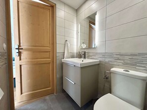 A bathroom with a wooden door, a white sink, a mirror, and a toilet. - Pixy Central and quiet area near Basel (Saint-Louis)