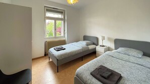 A bedroom with a large bed, a smaller bed, a window, a radiator, and a desk with a lamp. - 1st Central 2 BR w/ Living room + 5mn from Basel (Saint-Louis)
