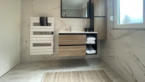 A modern bathroom with a marble backsplash, a built-in vanity with a mirror, and a window providing natural light.