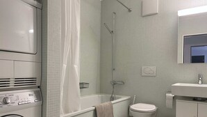 Et lille badeværelse med vaskemaskine, badekar, toilet og håndvask.