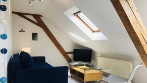 A modern loft bedroom with a sloped ceiling, a skylight, a blue sofa, a TV, and a wooden cabinet. - 3rd Central 1 BR w/ 3 single beds 45m2 + 5mn from Basel (Saint-Louis)