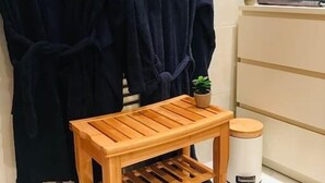 A bathroom with two dark blue robes hanging on a rack, a wooden stool with a plant on top, and a stack of folded towels on a shelf. - 3rd Central 1 BR w/ 3 single beds 45m2 + 5mn from Basel (Saint-Louis)