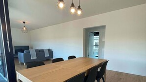 A modern dining area with a wooden table and black chairs, a TV in the background, and a ceiling light fixture. - Modern Apt. near City & Airport Basel (Basel)