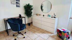 Une pièce comprenant un bureau, une chaise, une plante en pot, un miroir et une boîte de rangement colorée.