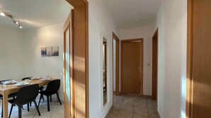 Un couloir avec un coin repas sur la gauche, comprenant une table et des chaises en bois, et une porte donnant sur une autre pièce.
