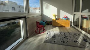 A balcony with a wooden floor, a red chair, a small table with toys, and a rug with a game design. - Modern 3 bedroom apartment near ISB and Basel (Reinach)