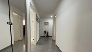 A hallway with tiled floors and white walls, leading to a room with a door. - Modern 3 bedroom apartment near ISB and Basel (Reinach)