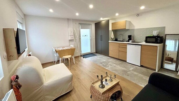 A compact living space with a sofa, a small dining table, a kitchen area with a microwave, and a TV mounted on the wall.