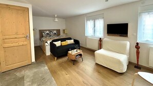 A spacious room with a bed, a sofa, a chair, and a TV mounted on the wall.