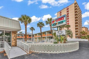 A Holiday Inn Express building with a sign welcoming guests, palm trees, and a brick wall. - Holiday Shores King Bed (Myrtle Beach)