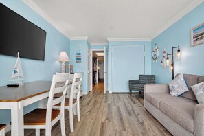 A room with a dining area, a sofa, and a hallway leading to another room. - Coral Beach Getaway, Oceanfront Pools & Lazy River (Myrtle Beach)