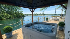 Een hottub op een houten terras met een touwbalk, uitkijkend op een rivier en bomen.