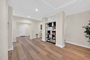 A spacious hallway with wooden flooring, white walls, and a black shelving unit with decorative items. - Grove Park Haven Sleeps 12, Large Backyard (Atlanta)