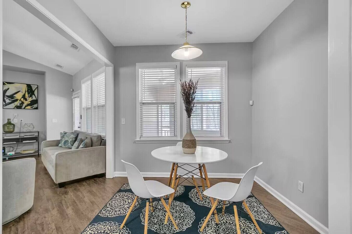 A dining area with a round table, two white chairs, and a vase of dried plants.