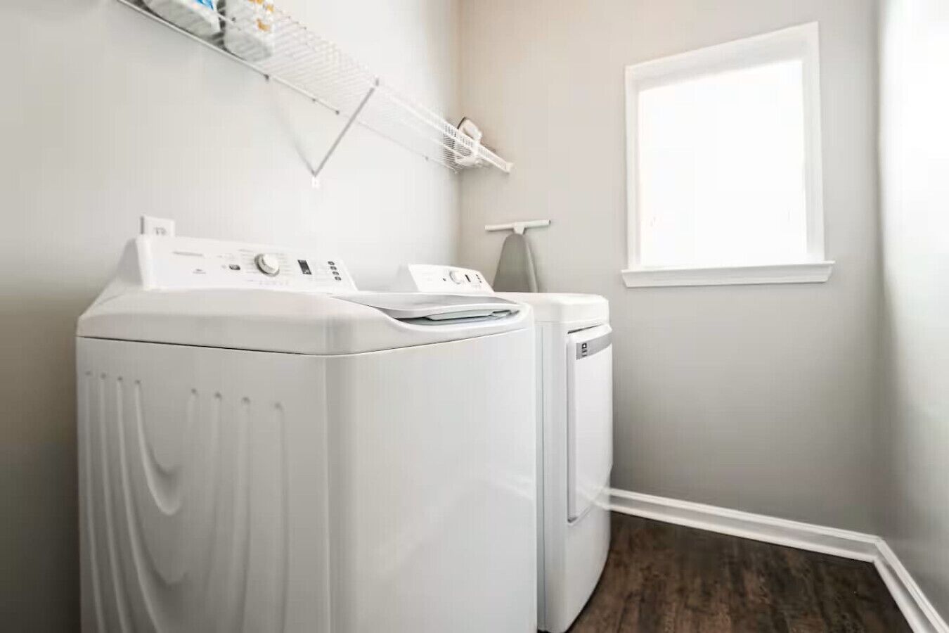 A laundry room with two white front-loading washing machines, a drying rack, and a window.