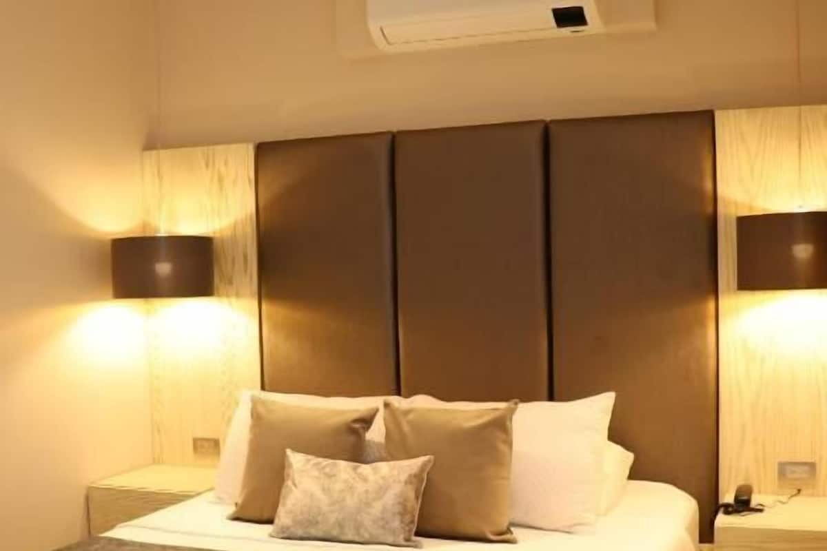 A hotel room with a bed, bedside lamps, an air conditioning unit, and a ceiling fan.