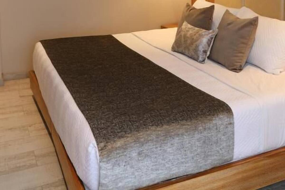 A bedroom with a bed, a ceiling fan, a wall-mounted air conditioner, and a bedside lamp.