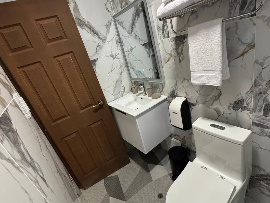 A bathroom with marble-patterned walls, a wooden door, a white sink, a toilet, and a towel rack with towels.