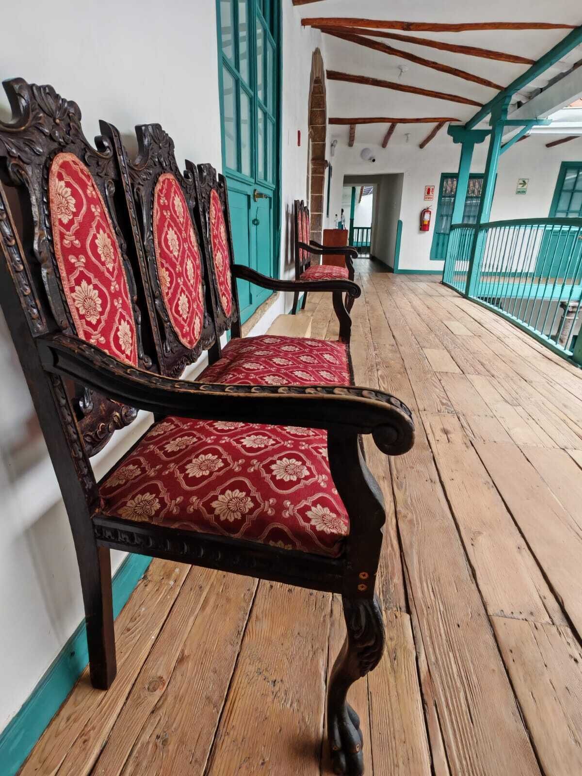 A wooden bench with red patterned upholstery in a corridor with teal accents and wooden flooring.