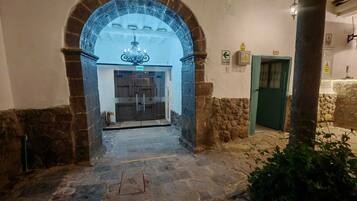 Una entrada arqueada con candelabro, paredes de piedra y una puerta verde.