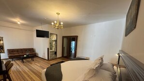 Une chambre à coucher avec un grand lit, un plancher en bois, un canapé, une télévision et un lustre.