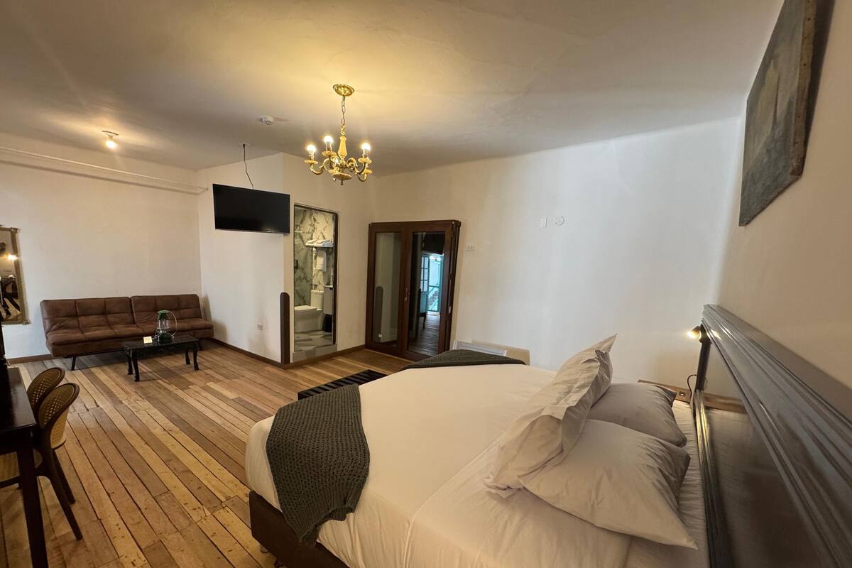 A bedroom with a large bed, a wooden floor, a sofa, a TV, and a chandelier.