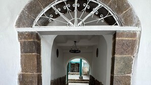 Un chemin de pierre mène à une porte en arc surmontée d’une grille décorative en métal.