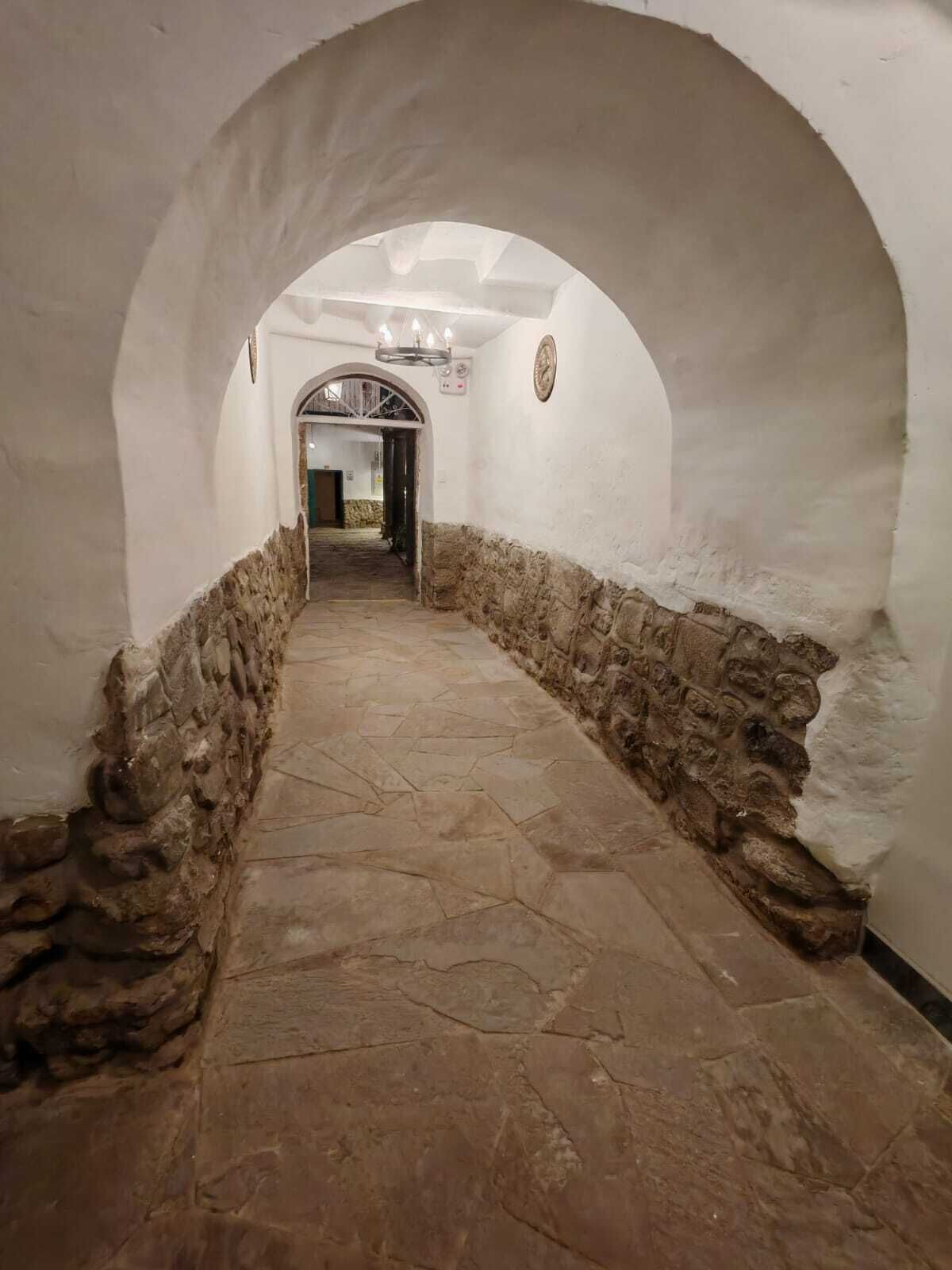 A corridor with stone walls and a tiled floor, leading to an arched doorway.