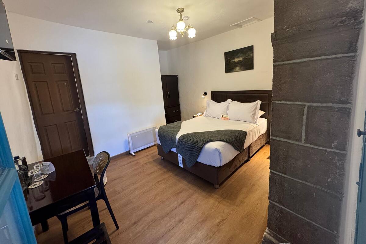 A bedroom with a bed, a desk, and a chair. There is a door and a window.