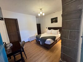 Un dormitorio con una cama, un escritorio y una silla. Hay una puerta y una ventana.