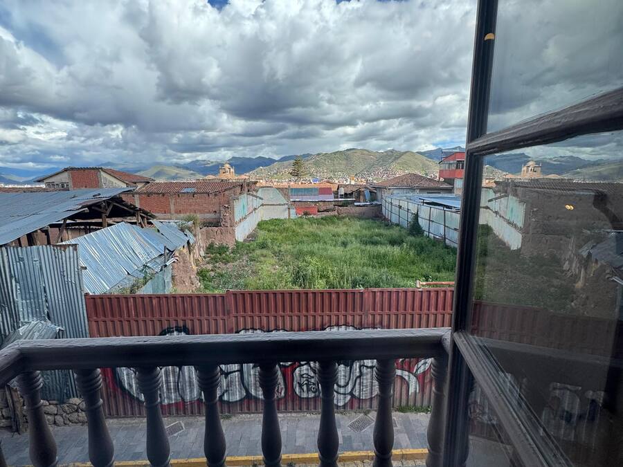 A view from a window with a metal railing, overlooking a town with buildings and a mountain in the background.