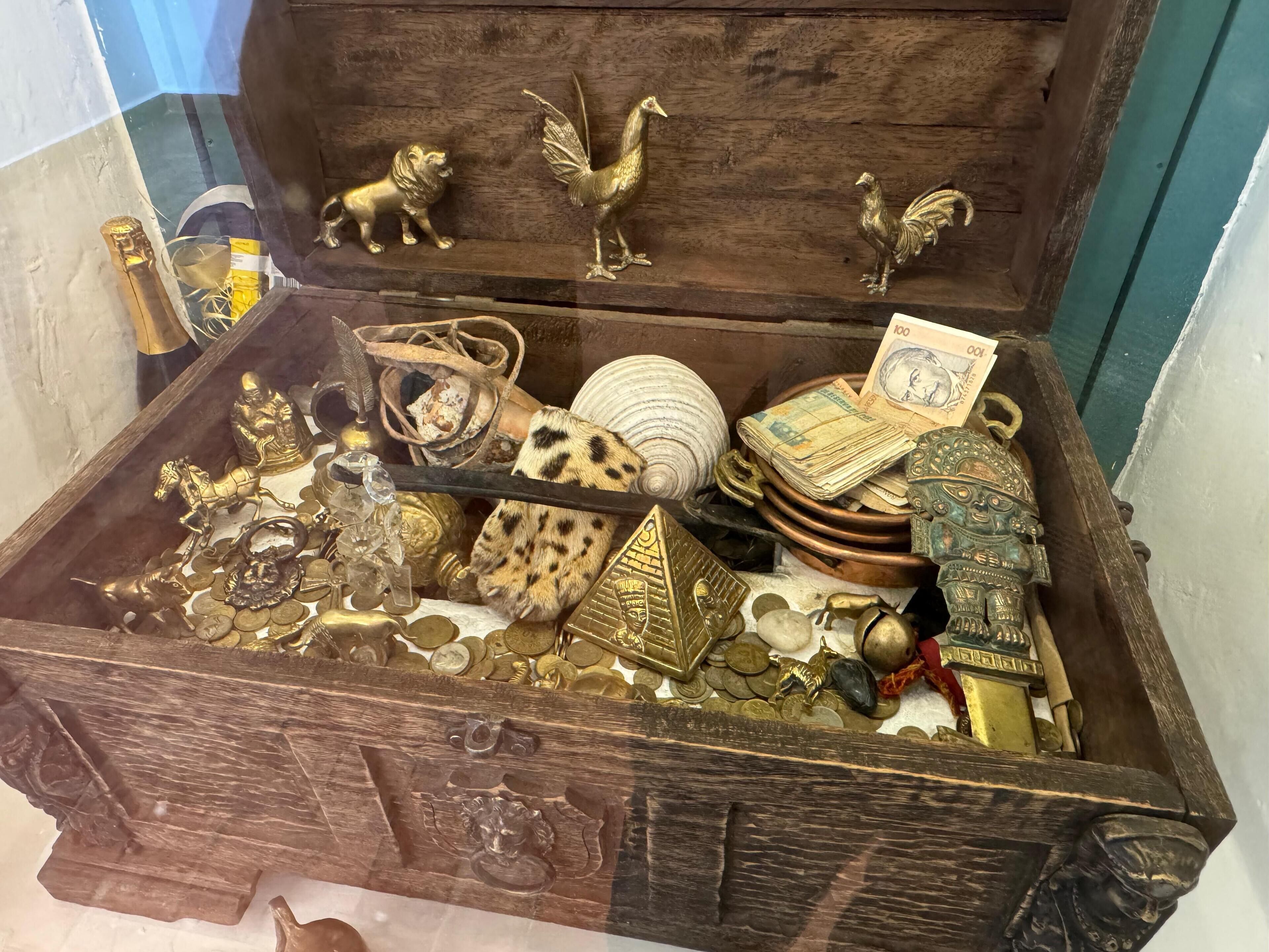 A wooden chest filled with various items including coins, jewelry, and decorative objects.