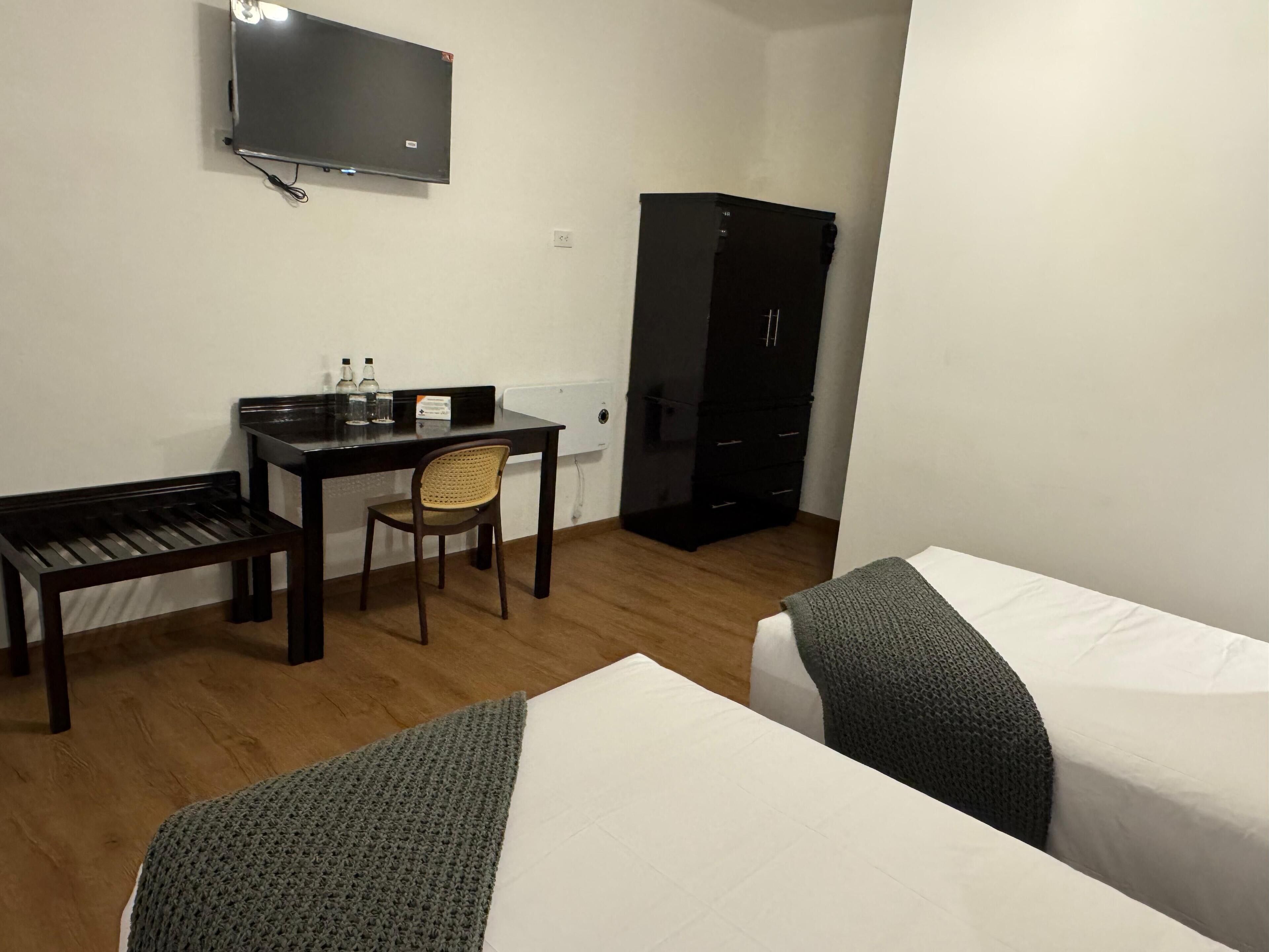 A hotel room with a desk, chair, two beds, a TV, and a wardrobe.