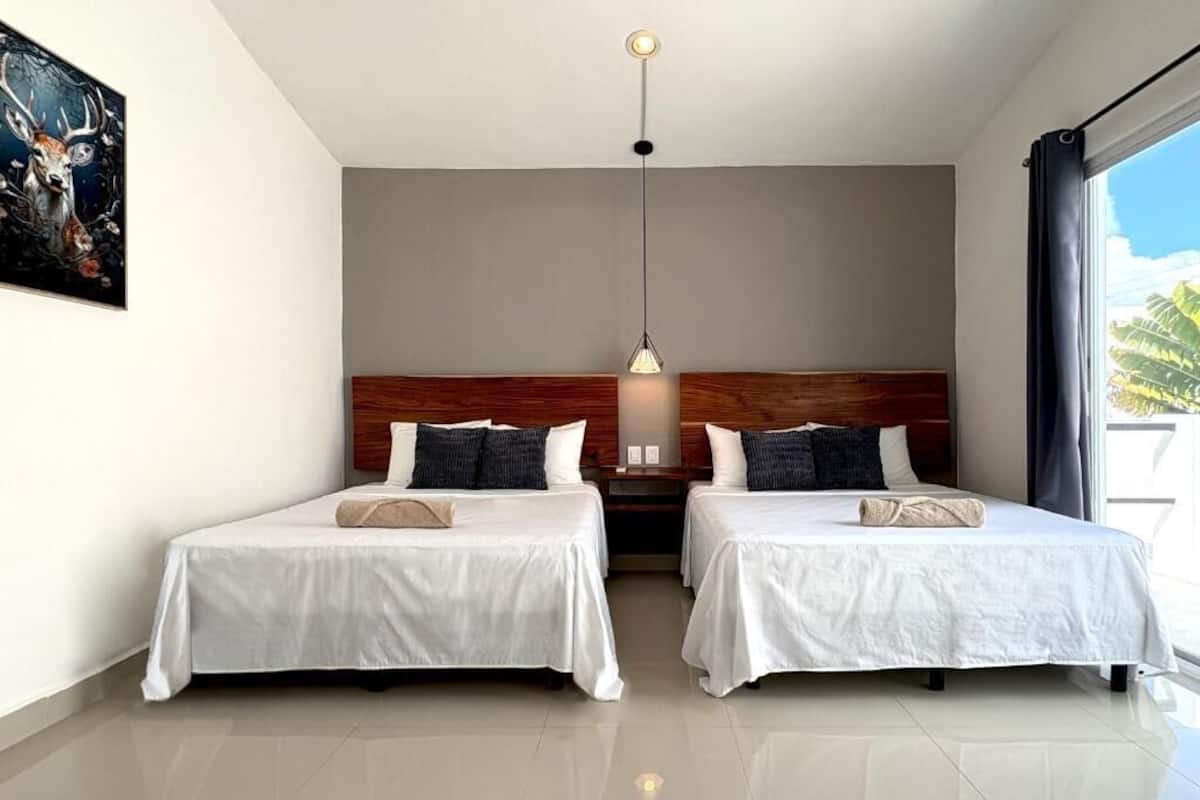 Een hotelkamer met twee bedden, een houten hoofdeinde, een hanglamp en een groot raam met gordijnen.
