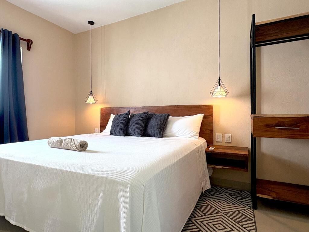 A neatly made bed with a white bedspread and two pillows, a wooden nightstand with a lamp, and a wardrobe with a mirror.