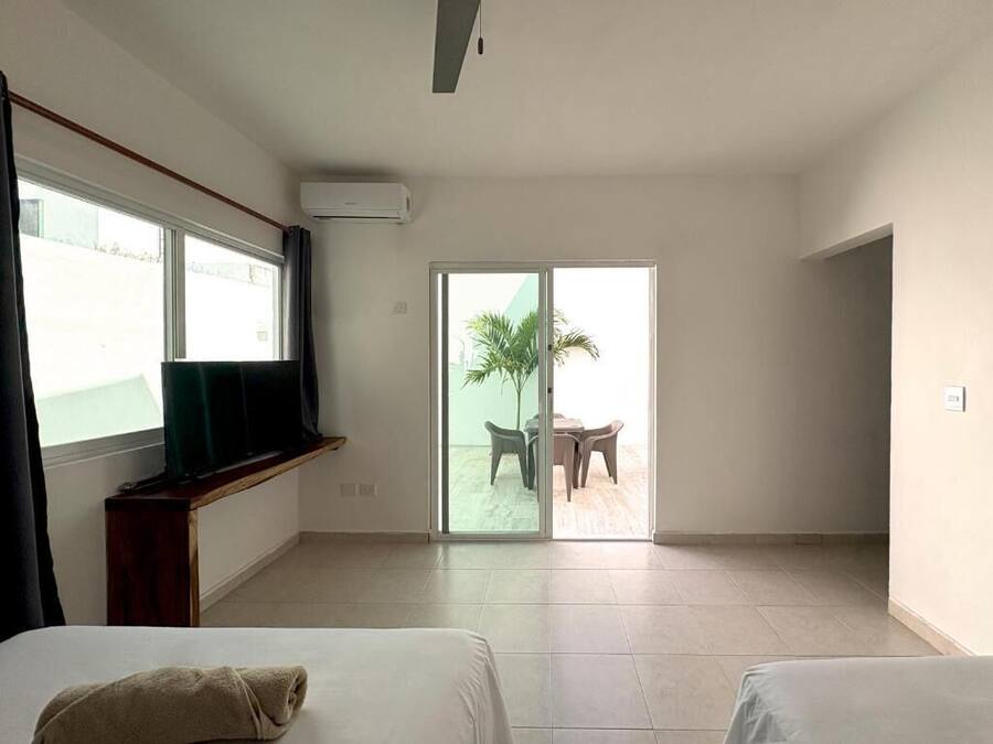 A hotel room with two beds, a TV, an air conditioner, and a sliding glass door leading to an outdoor area with a table and chairs.