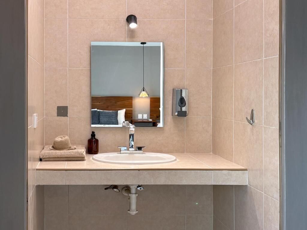 A modern bathroom with a beige tiled wall, a white sink, a mirror, and a towel on the counter.