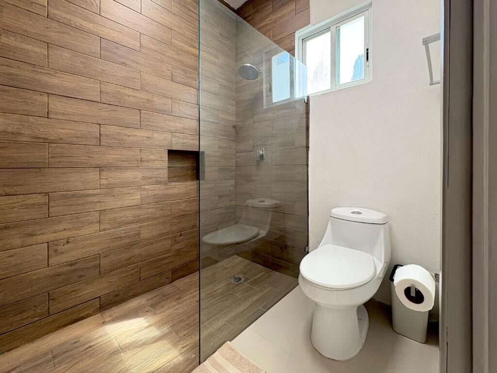 A bathroom with a wooden wall, a glass shower enclosure, a white toilet, and a small window.