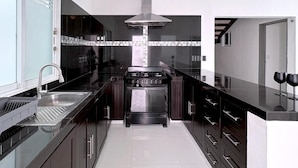 Une cuisine moderne avec des meubles de couleur sombre, une hotte de cuisine en acier inoxydable et un îlot central doté d’un évier et de verres à vin.