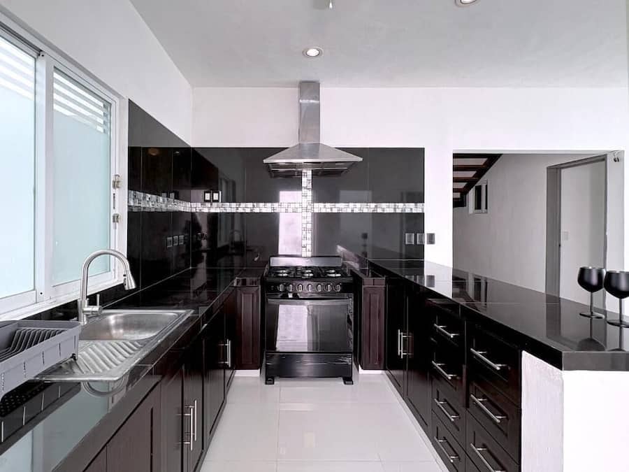 A modern kitchen with dark cabinetry, a stainless steel range hood, and a central island with a sink and wine glasses.