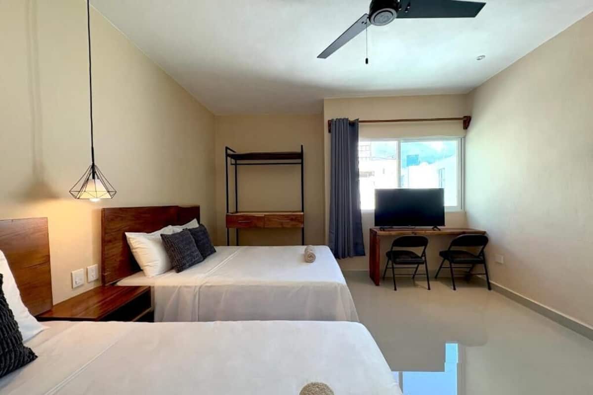 Een hotelkamer met twee bedden, een bureau, een televisie en een plafondventilator.