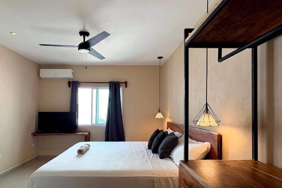 Een hotelkamer met een bed, een bureau, een plafondventilator, een televisie en een raam met gordijnen.