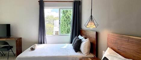 A hotel room with two beds, a desk, a television, and a window with curtains.