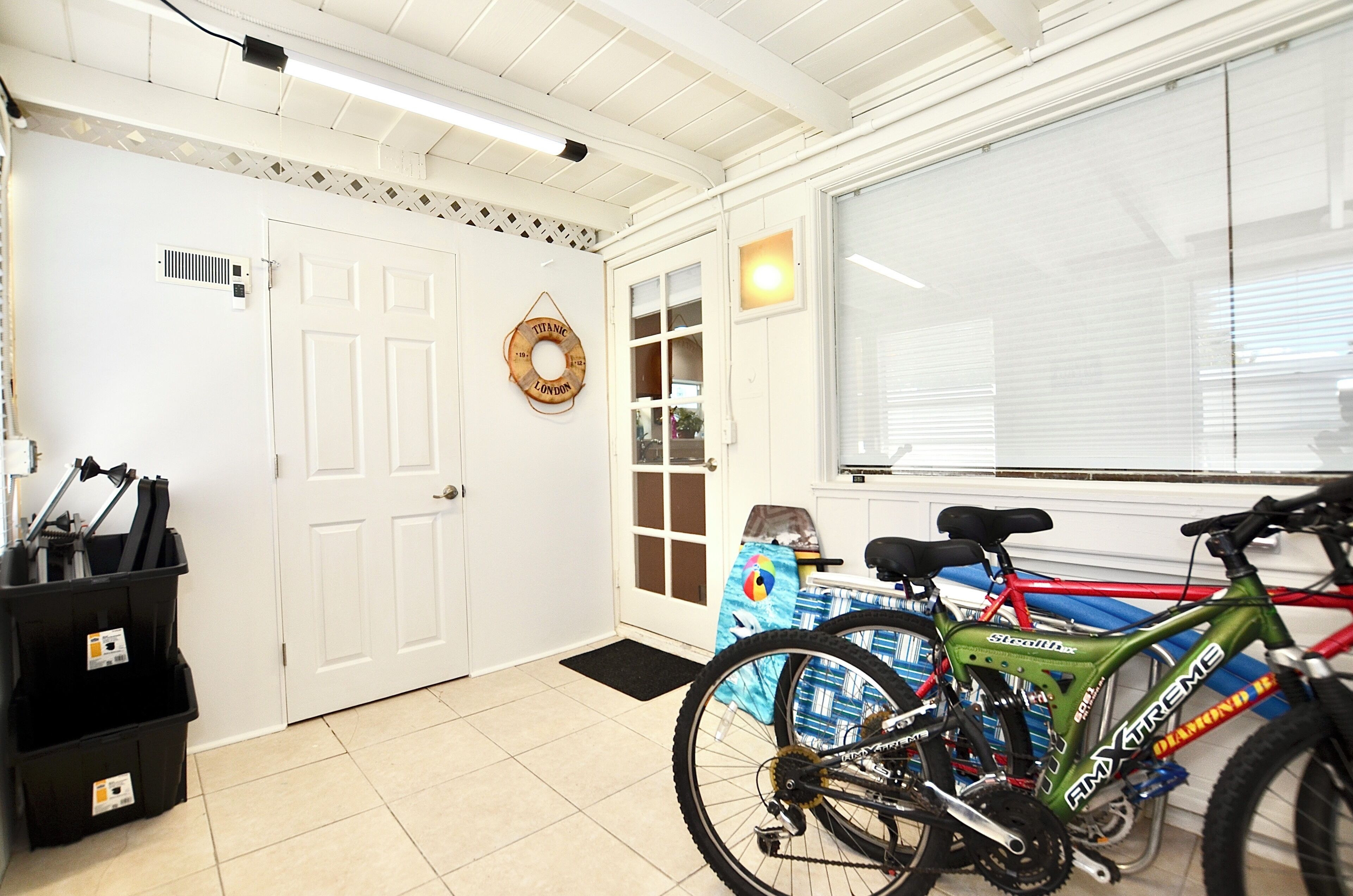 Un espace intérieur propre et bien éclairé, avec une porte blanche, une fenêtre équipée de stores et un vélo appuyé contre le mur.