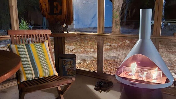 Un'atmosfera accogliente con soffitto in legno, una poltrona imbottita, un camino in vetro e vista sull'esterno.