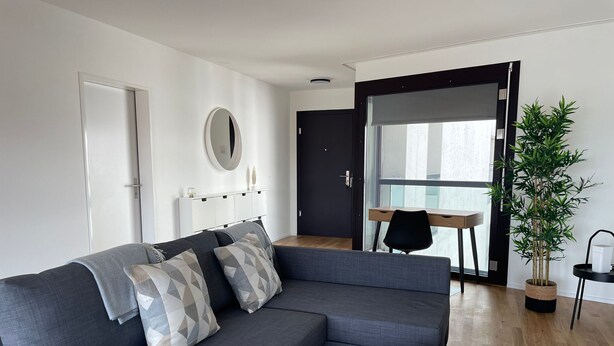 A modern living room with a grey sectional sofa, a round wooden coffee table, and a potted plant. - Top modern Apartment near Novartis Campus (Basel)
