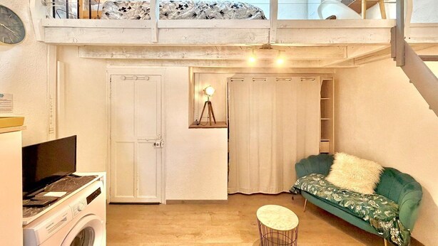 Un appartement de style « loft » comprenant un lave-linge, un canapé vert, une petite table ronde et un escalier menant à un niveau supérieur.