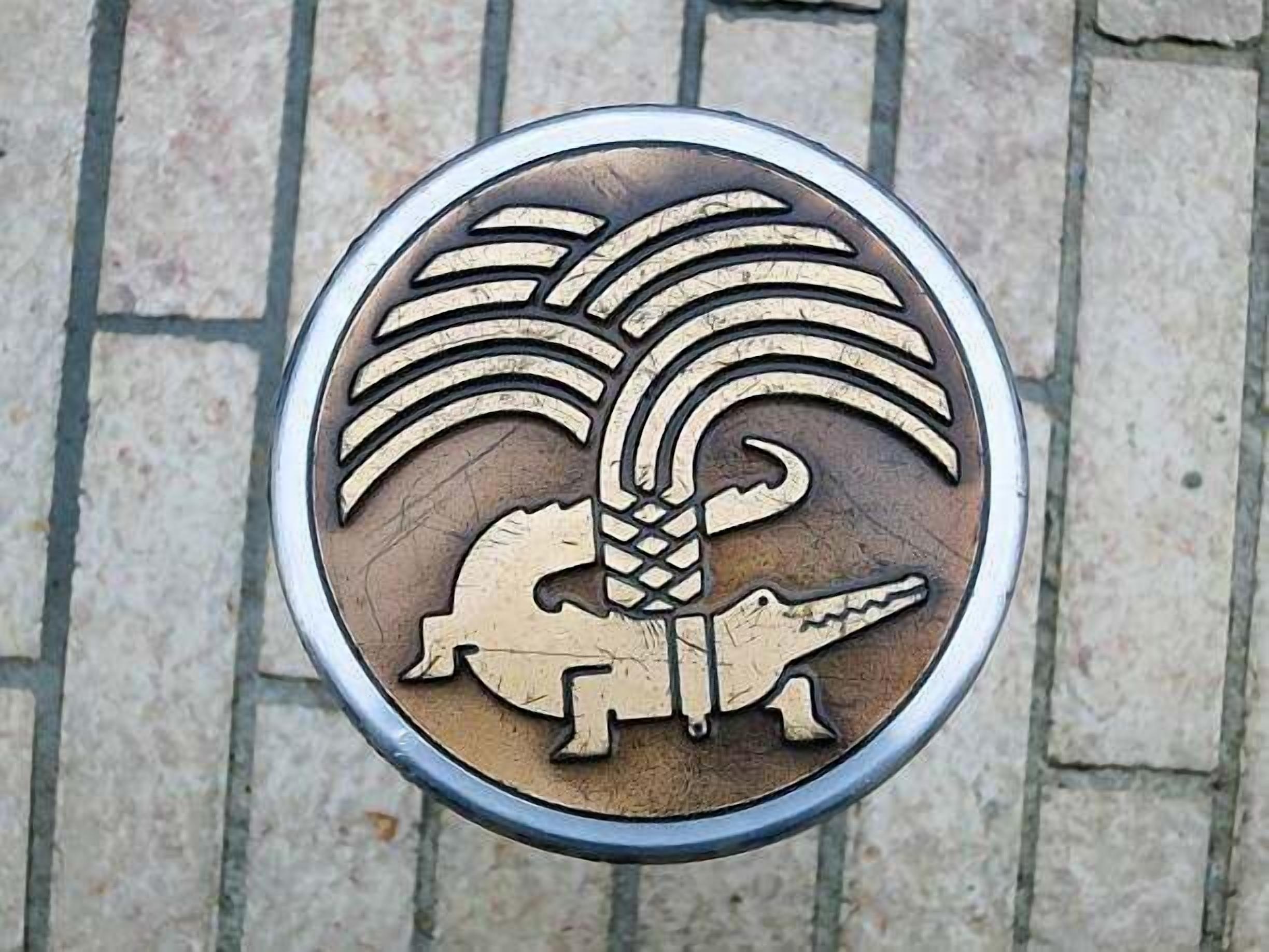 A circular emblem with a stylized palm tree and a crocodile.